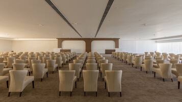 A large conference room with rows of chairs, a carpeted floor, and a high ceiling with ventilation ducts.