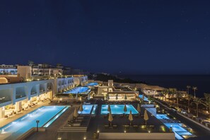 Ein Resort mit mehreren Schwimmbecken, Palmen und Blick auf das Meer bei Nacht.