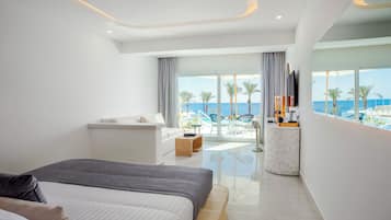 Una habitación de hotel moderna con una cama grande, un área de estar con vista al océano y un balcón con mobiliario exterior.
