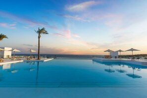 Zona junto a la piscina con sillones de descanso y sombrillas, con vista a un cuerpo de agua.