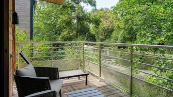 A wooden deck with a metal railing overlooking a river, surrounded by lush greenery.
