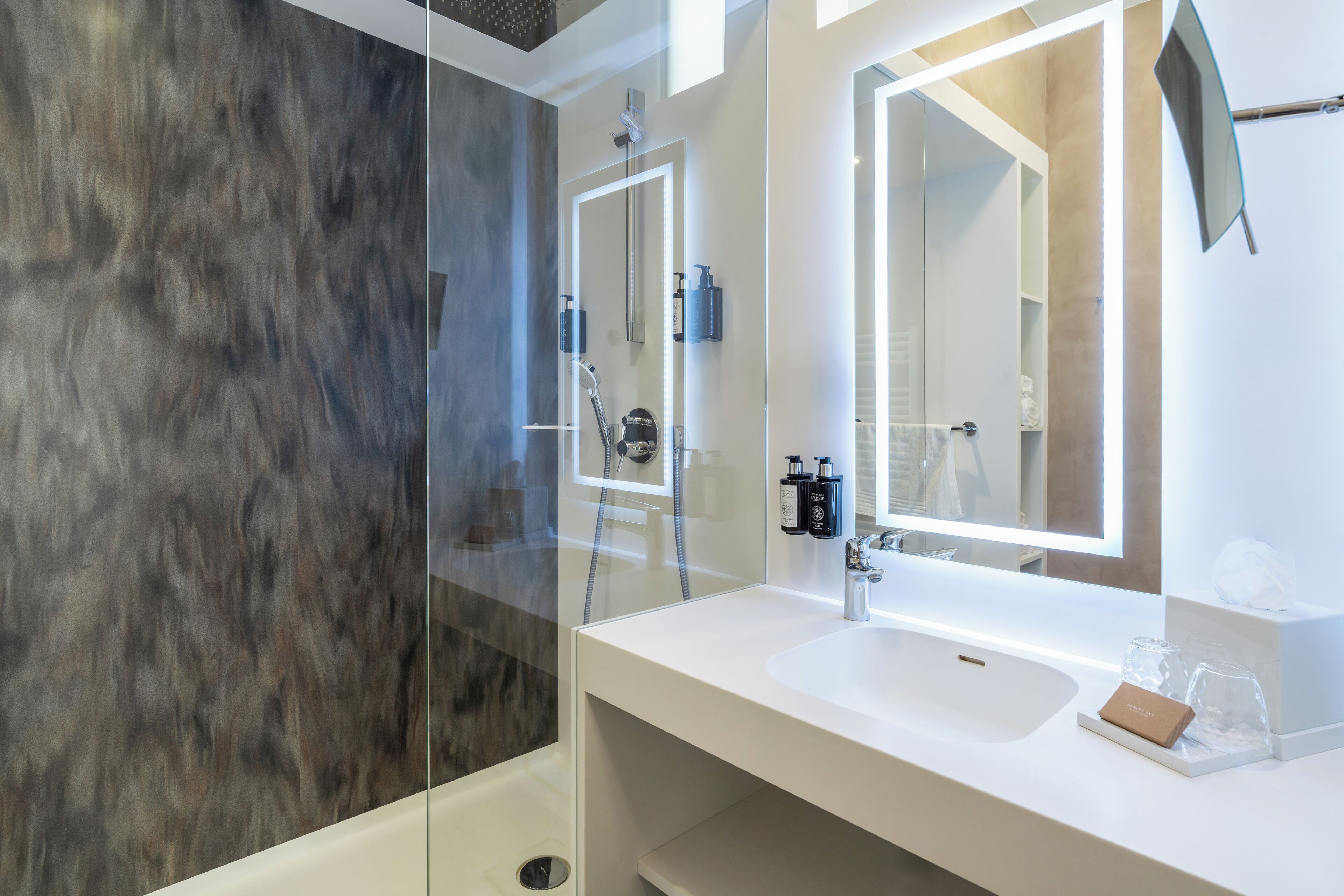 Un baño moderno con ducha de vidrio, lavamanos blanco y un espejo grande.