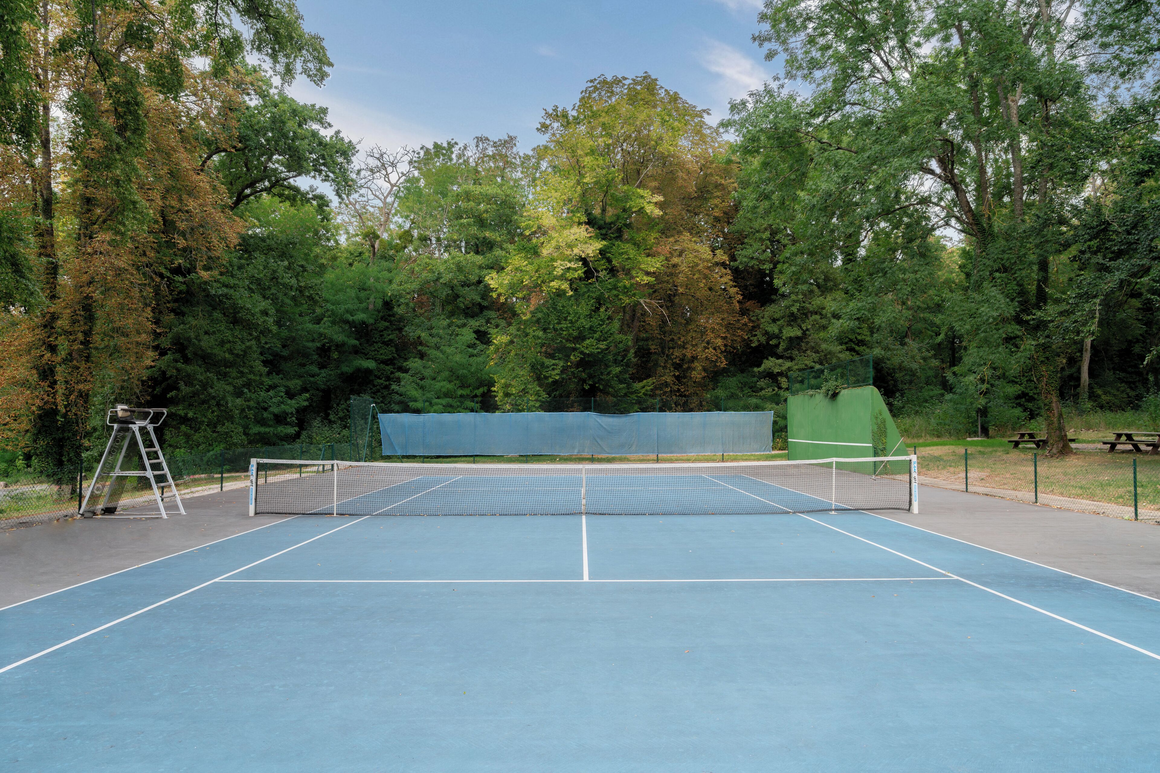 An outdoor tennis court surrounded by trees.