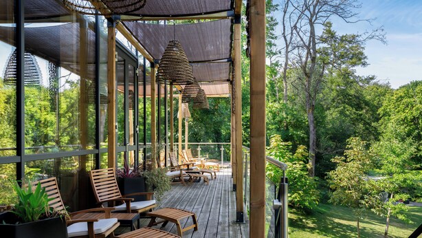 Puinen terassi ulkokalusteineen, köynnöksillä koristeltu pergola, joka tarjoaa varjoa, ja näkymä vehreään maisemaan.