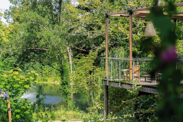 A wooden deck with glass railings overlooking a lake, surrounded by lush greenery. - Domaine de la Résidence Hotel Spa & Restaurant (Moulins-lès-Metz)