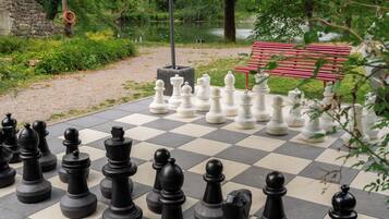 A large outdoor chessboard set up in a park with a bench in the background.