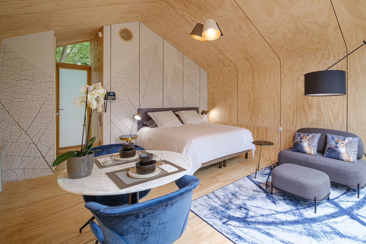 Un dormitorio moderno con una cama, un sofá, una mesa de comedor con sillas y una planta decorativa.