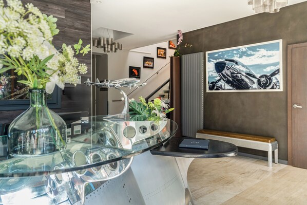 Un interior moderno con una mesa de centro de vidrio, un banco y una foto enmarcada de un avión en la pared.