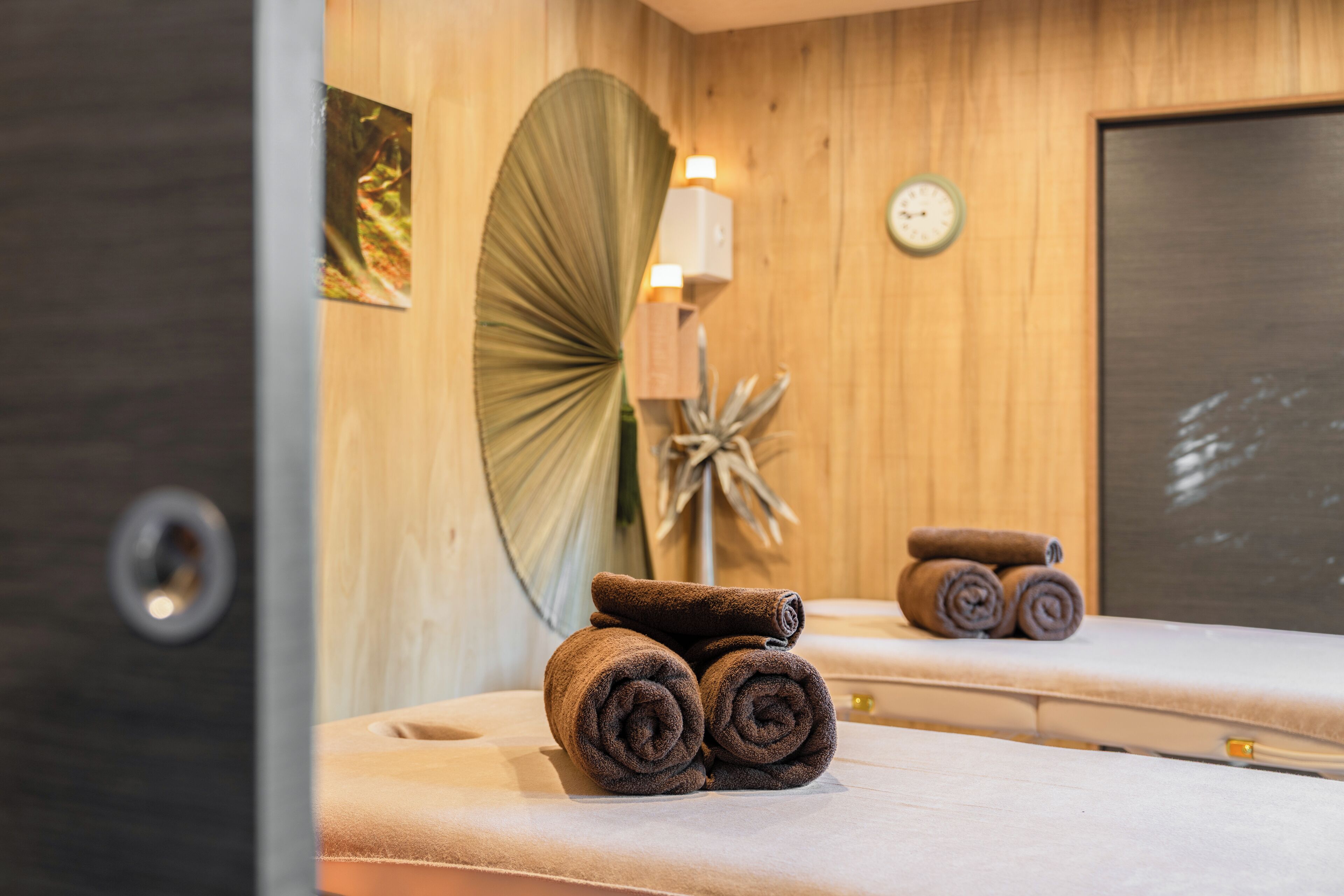 A room with wooden walls, a large fan, a clock, and towels on a table.