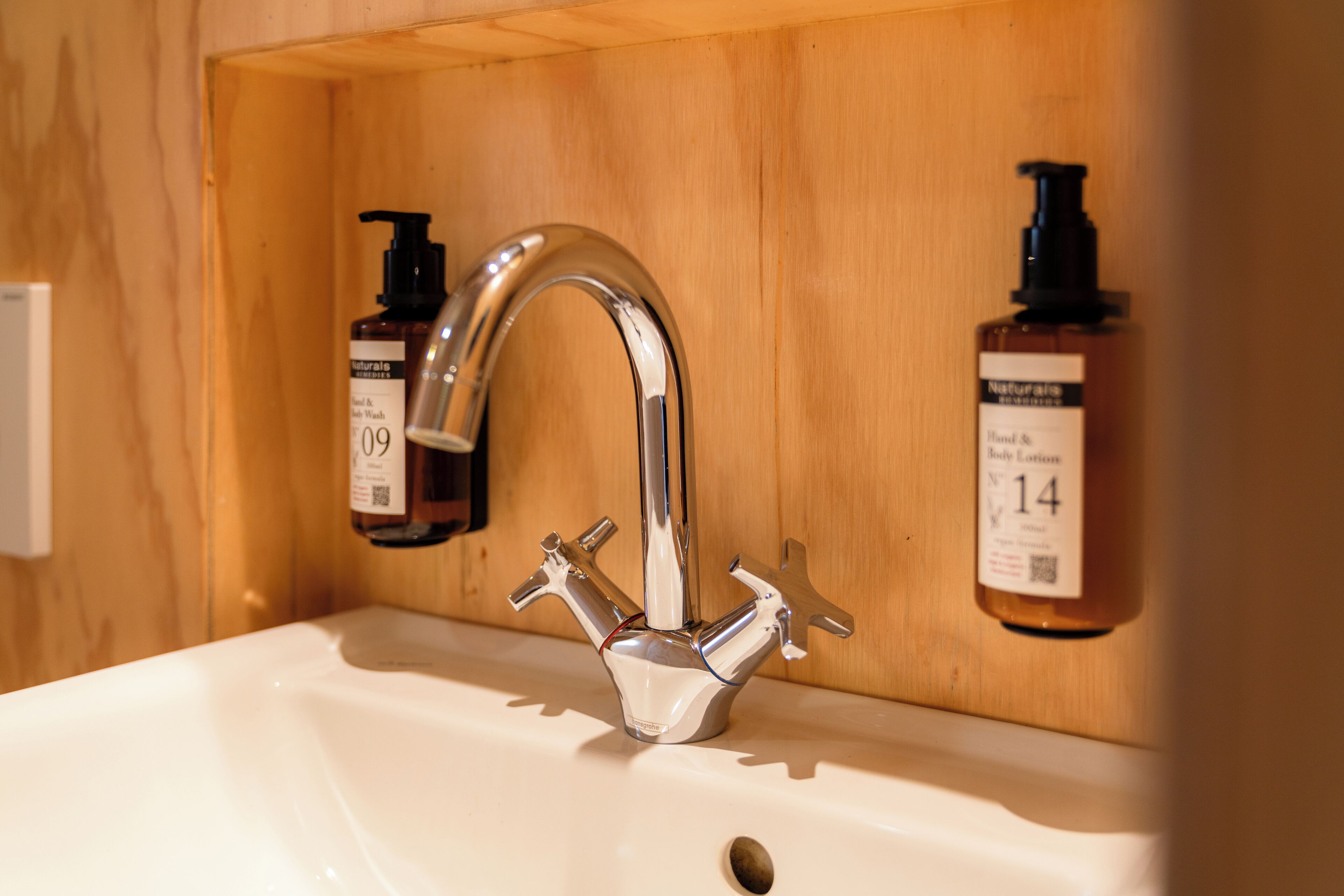 Ein Badezimmerwaschbecken mit Chromarmatur, zwei Seifenspendern und einer Holzvertäfelung im Hintergrund.