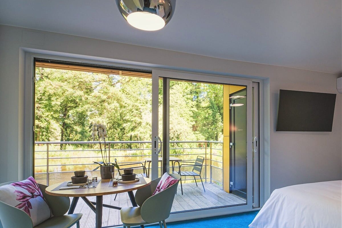 Habitación de hotel con balcón, una cama, una mesa con sillas y una lámpara de techo.