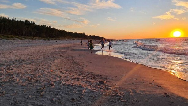 En strand där folk promenerar längs strandkanten under solnedgången.