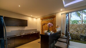 A modern kitchen with dark cabinetry, a built-in oven, and a large window overlooking a stone wall and tropical plants. - Green Oasis Private Villa (Ubud)