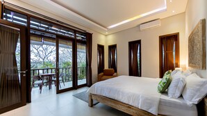 A bedroom with a large bed, a balcony with a table and chairs, and a view of trees. - Green Oasis Private Villa (Ubud)