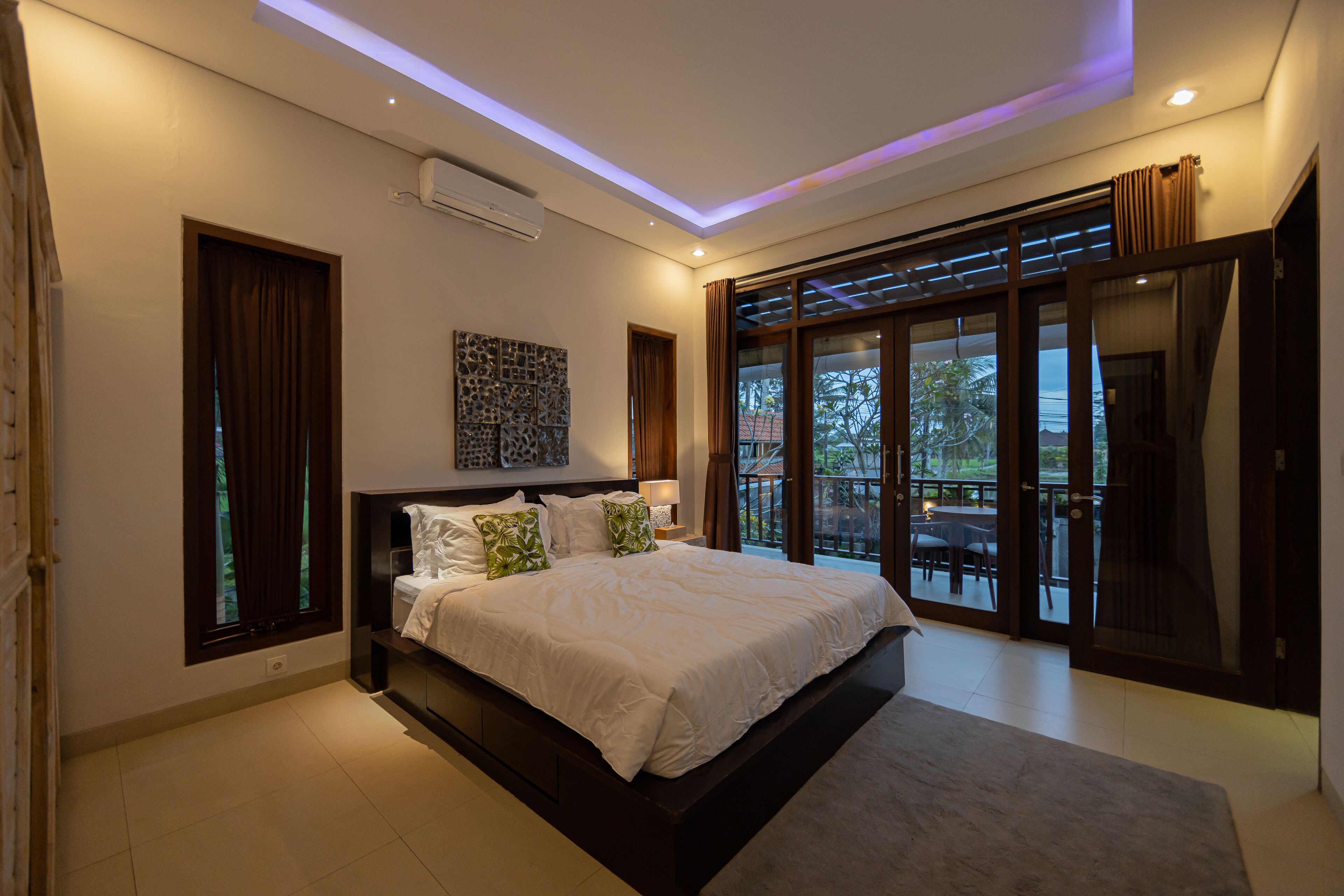 A modern bedroom with a large bed, a ceiling light, and a view of the outdoors.