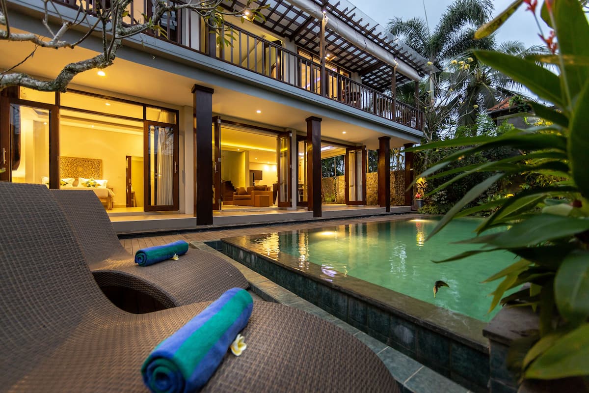 Un espace aménagé au bord de la piscine, avec des chaises longues et une piscine, le tout entouré d’une végétation luxuriante.