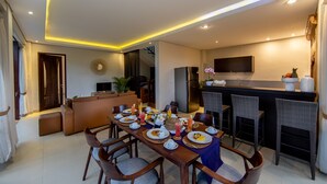 A modern living room with a dining area, a kitchen, and a TV mounted on the wall. - Green Oasis Private Villa (Ubud)
