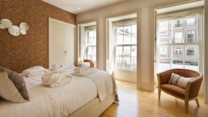 A hotel room with a large bed, a sitting area with a chair, and a view of the city through the windows. - Amazing 2 Bedroom Apt w/ Great Views, 2 min Walk From Douro River in City Center (Porto)