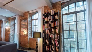 Habitació amb parets de maó a la vista, grans finestres, una biblioteca i una làmpada.