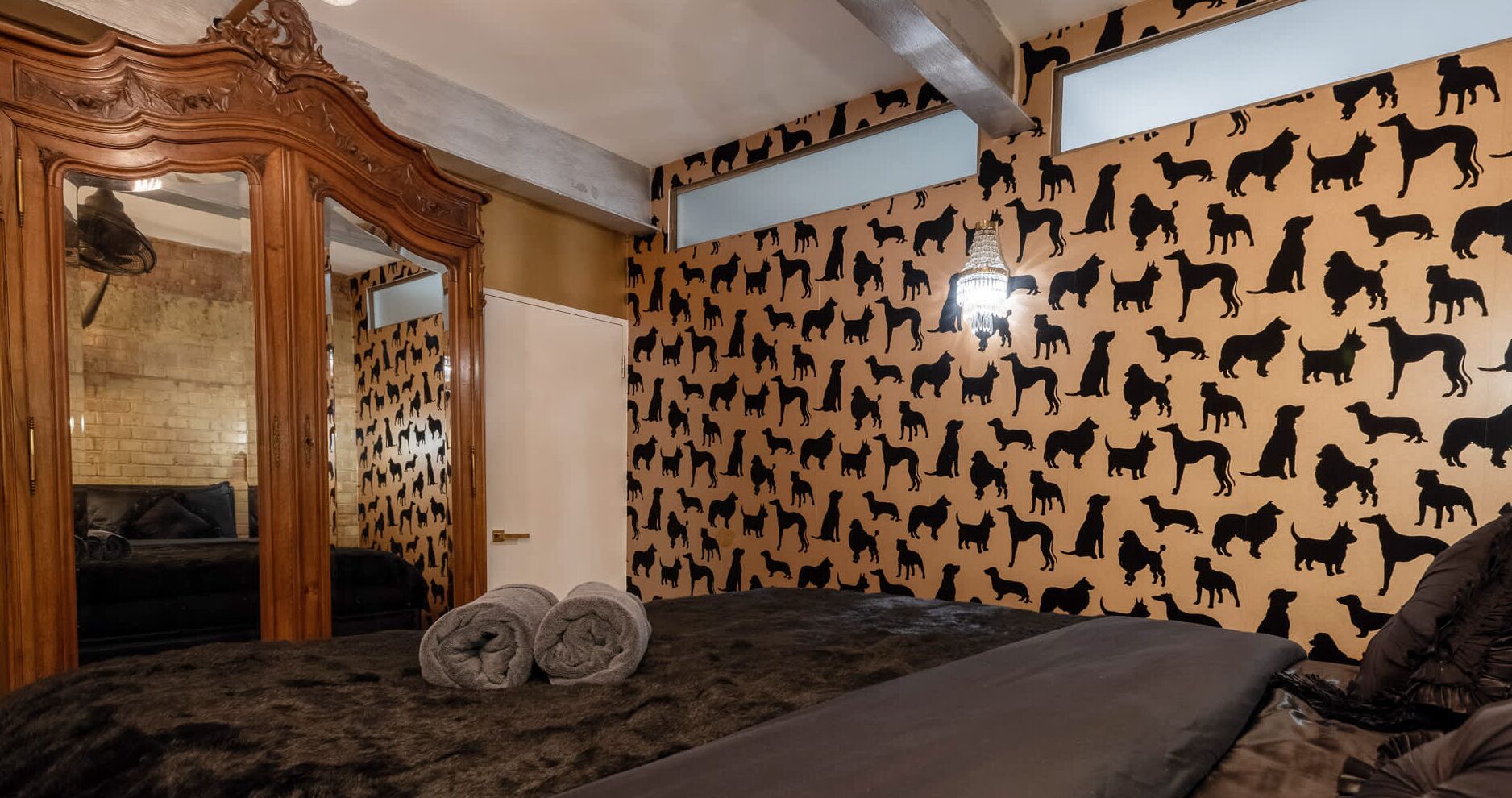 Un dormitorio con pared estampada, un armario de madera, una cama con toallas dobladas y un candelabro.