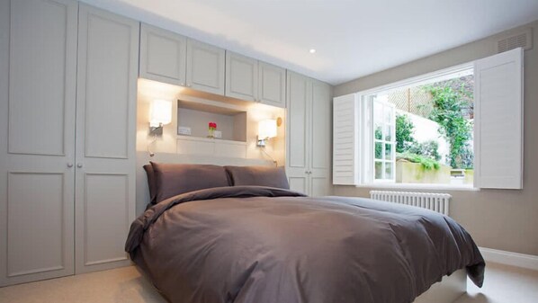 Ein Schlafzimmer mit einem großen Bett, integriertem Kleiderschrank und einem Fenster mit Fensterläden.