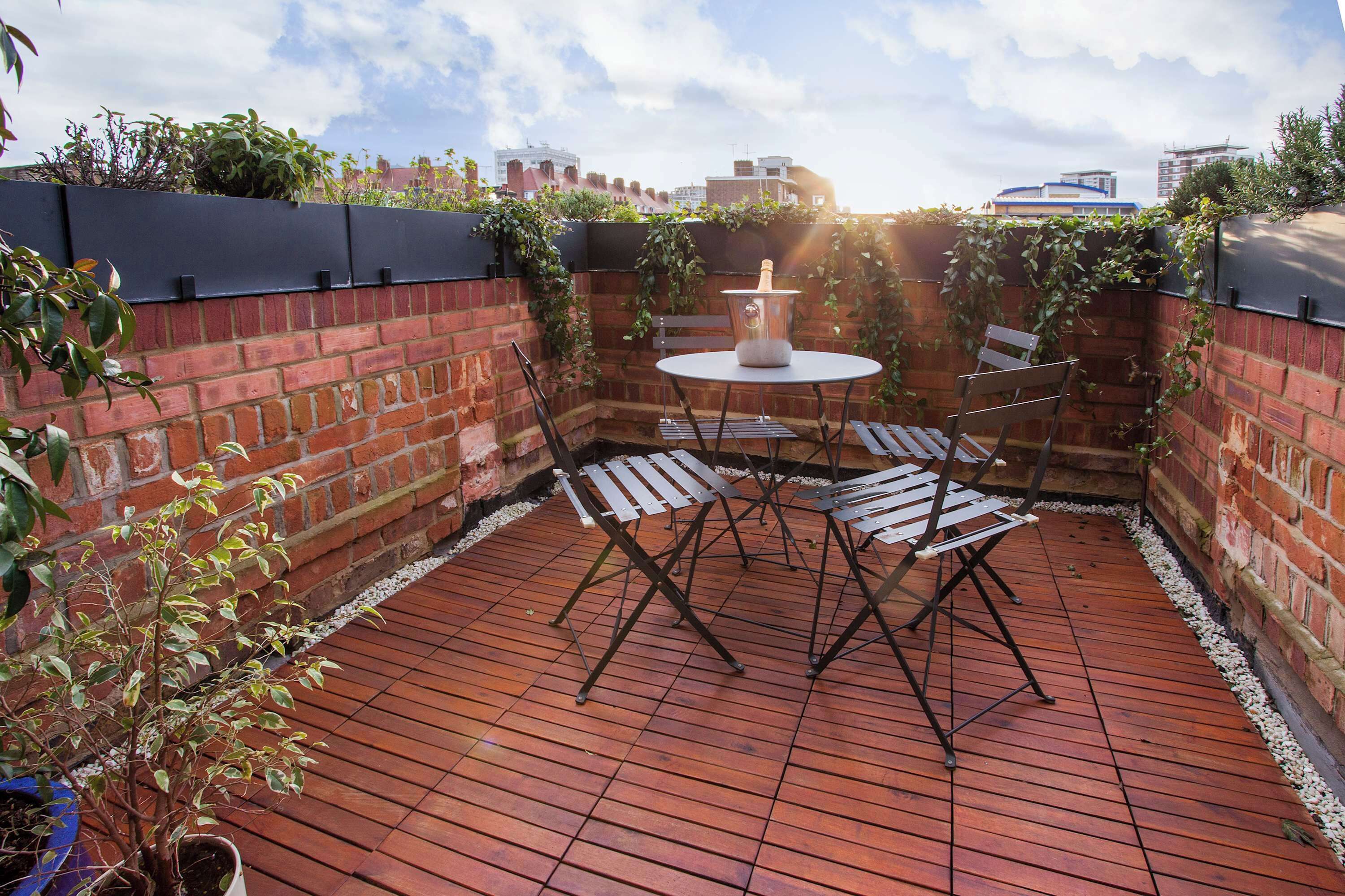 Een terras met een bakstenen muur, een ronde tafel en vier stoelen.