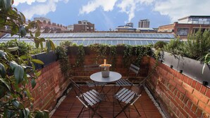 Una terrazza sul tetto con tavolo e sedie, circondata da muri in mattoni e piante.