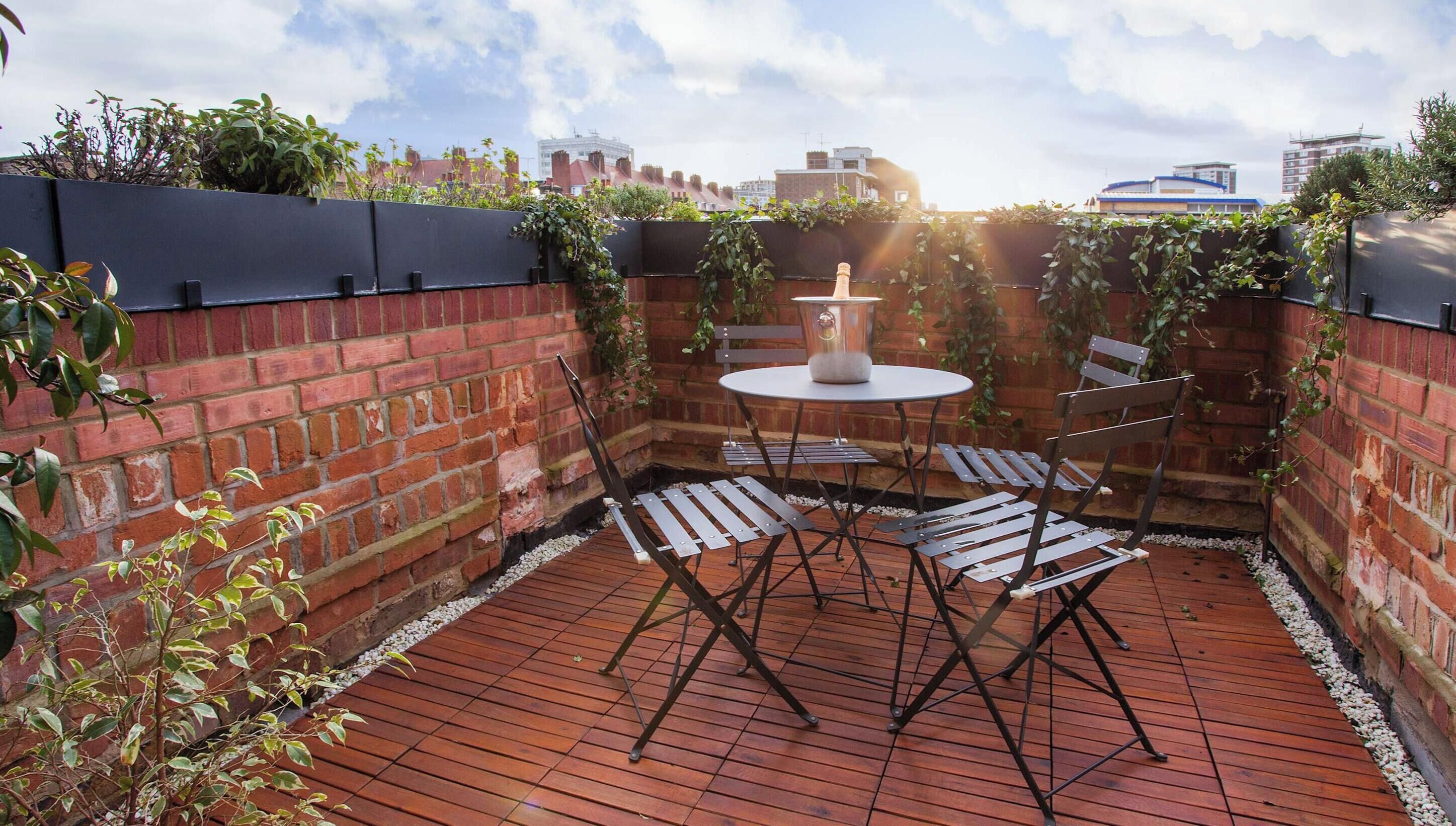 A rooftop patio with a brick wall, a round table, and metal chairs.