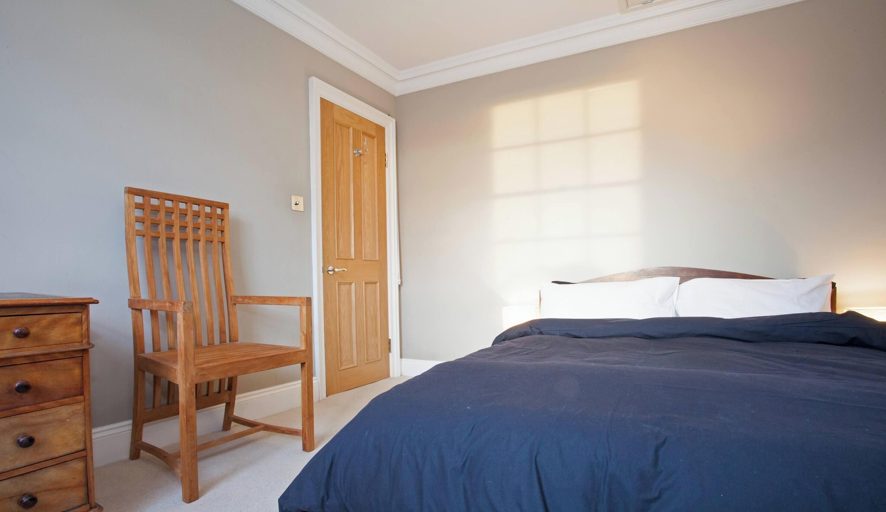 Une chambre à coucher avec un lit, une chaise en bois et une commode.