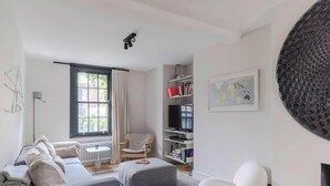 A modern living room with a sofa, ottoman, chair, bookshelf, and a large circular wall decoration. - Stylish IslingtonTownhouse with Terrace & Garden (Greater London)