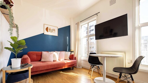 A living room with a red sofa, a round table, a black chair, a potted plant, and a mounted TV.