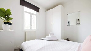 A bedroom with a bed, a radiator, a window with a blind, a mirror, and a potted plant.