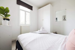 A bedroom with a bed, a radiator, a window with a blind, a mirror, and a potted plant. - 1 Bedroom Flat - Shepherds Bush (Greater London)