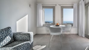A modern living room with a patterned sofa, a round dining table with chairs, and large windows with curtains. - NiMa Sifnos Residences (Sifnos)