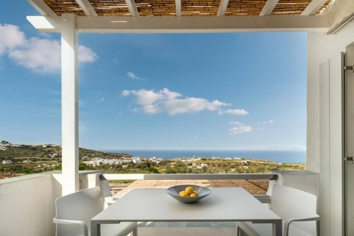 A balcony with a table and chairs, a bowl of lemons, and a view of the sea and landscape.