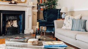 Uma sala de estar aconchegante com lareira, uma poltrona azul escura, um sofá bege e uma estante cheia de livros.