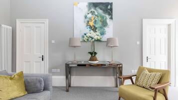 A living room with a grey sofa, a yellow armchair, a console table with two lamps, and a large abstract painting on the wall.