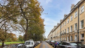 Eine Straße gesäumt von parkenden Autos und Bäumen mit Herbstlaub.