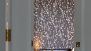 Ein Schlafzimmer mit gemustertem Wandpapier, einem Bett mit Kopfteil, Kissen und einem Nachttisch mit Büchern.