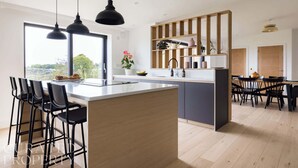 Een moderne keuken met een centraal eiland, zwarte barkrukken en hanglampen.