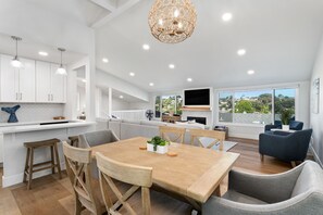 Una cocina moderna con armarios blancos, una mesa de comedor de madera y un gran ventanal con vistas al exterior.
