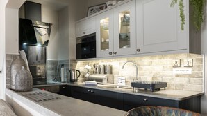 A modern kitchen with a built-in oven, stainless steel appliances, a sink, and a decorative bowl. - Harbour View - Flat 2 - Tudor House (Barmouth)