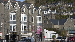 A row of stone buildings with multiple stories, featuring various shops and businesses on the ground floor, including a pizzeria. - Harbour View - Flat 2 - Tudor House (Barmouth)
