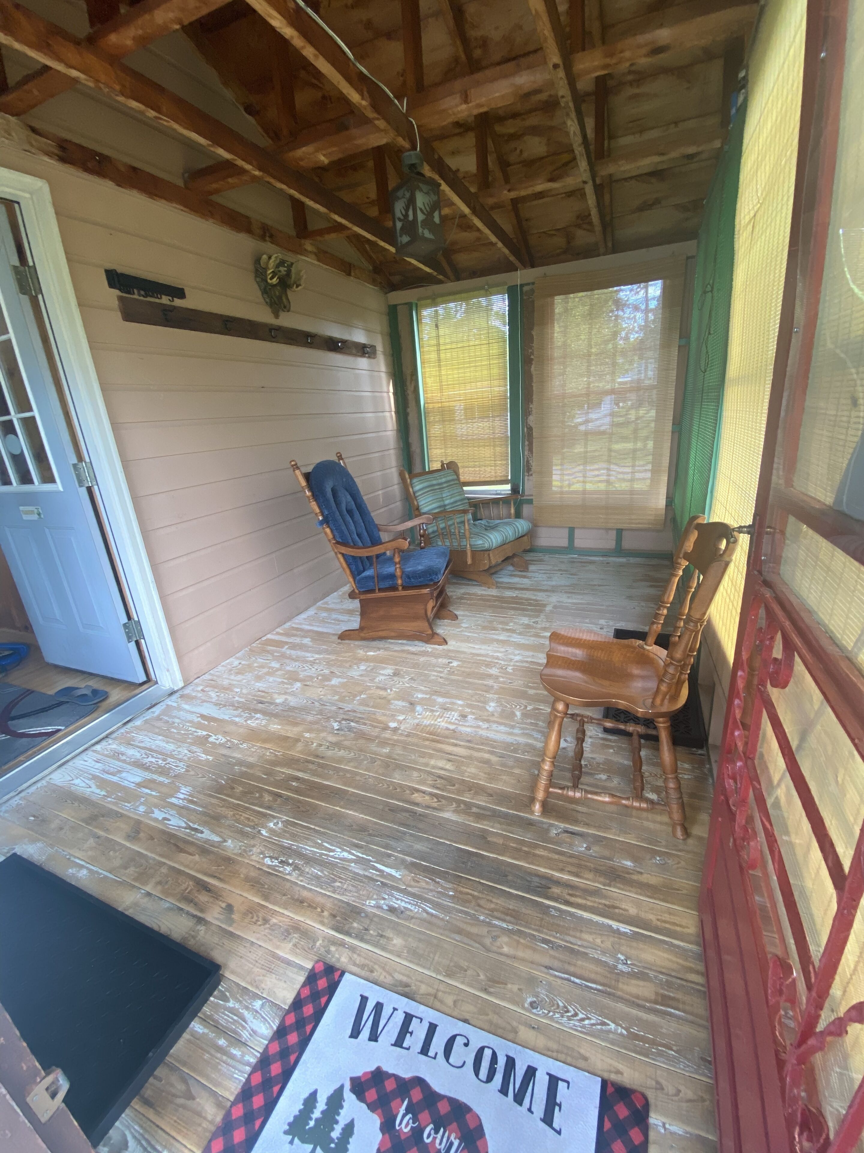 A wooden porch with a welcome mat, two rocking chairs, and a door.