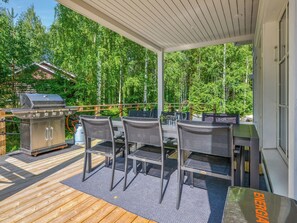 An outdoor deck with a grill, chairs, and a table.
