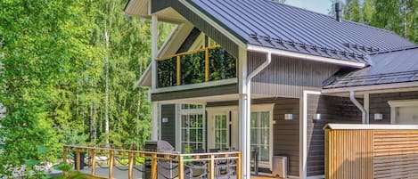 A two-story cabin with a deck, large windows, and a metal roof.