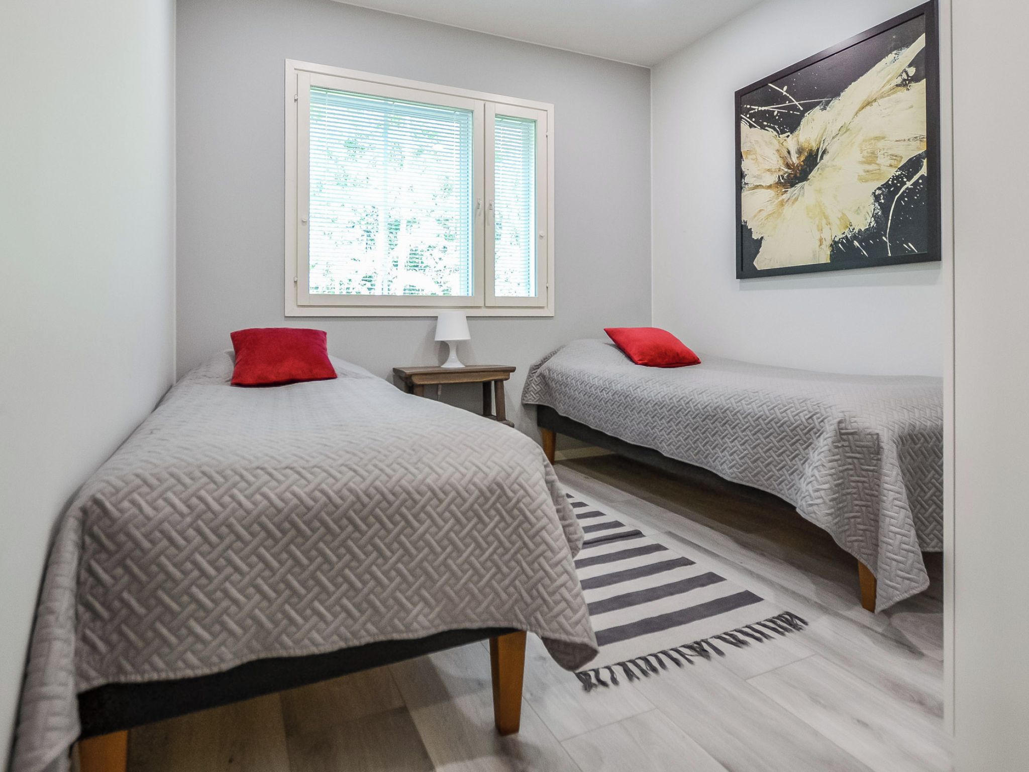 A room with two beds, a window, a lamp, and a painting.