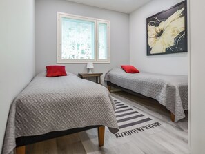 A room with two beds, a window, a lamp, and a painting.