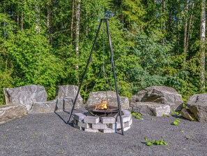 Montaje de fogata con una parrilla metálica y un brasero, rodeado de rocas y un bosque de fondo.