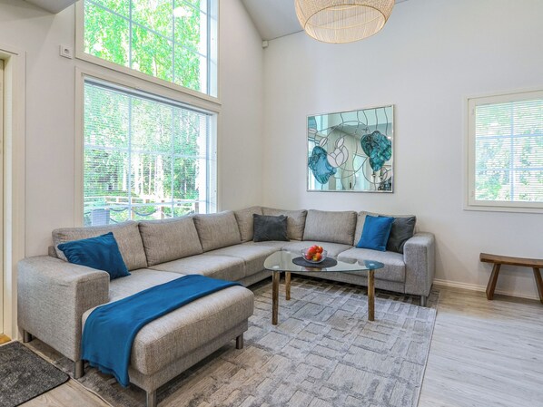 A modern living room with a sectional sofa, a glass coffee table, and a large window with blinds.